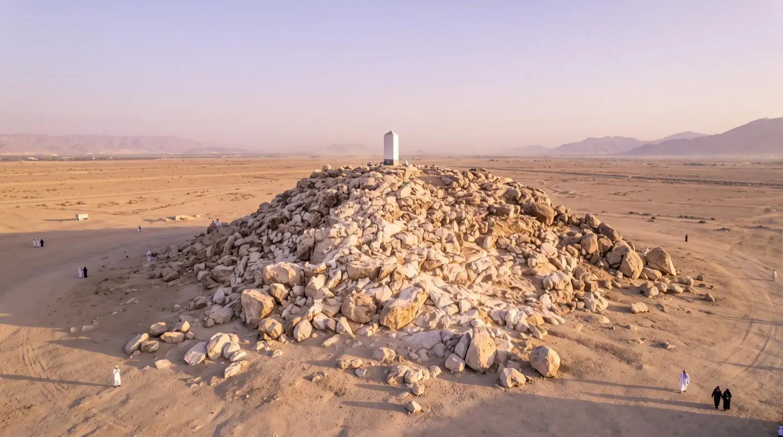The rocky hill of Jabal ar-Rahmah on the plain of Arafat at golden hour, with a white pillar at its summit and open desert around it.