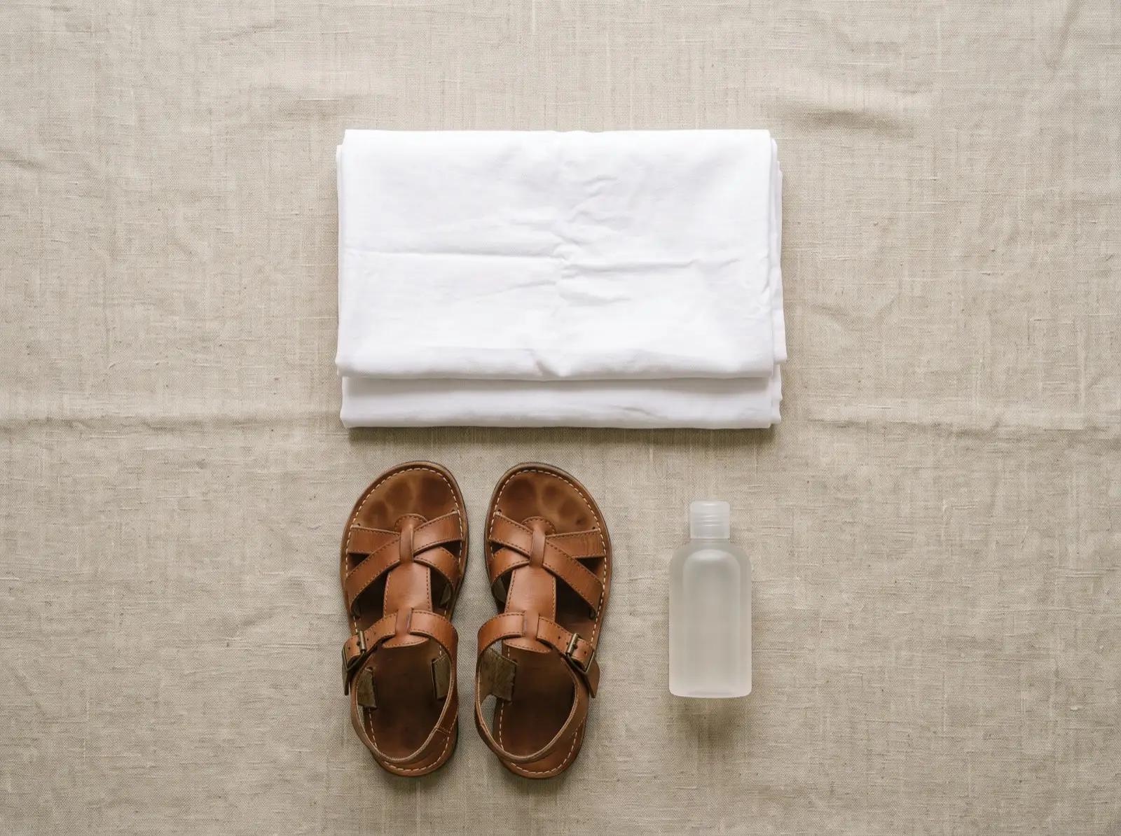 Two folded white ihram cloths, leather sandals and a bottle of unscented soap laid out on linen.